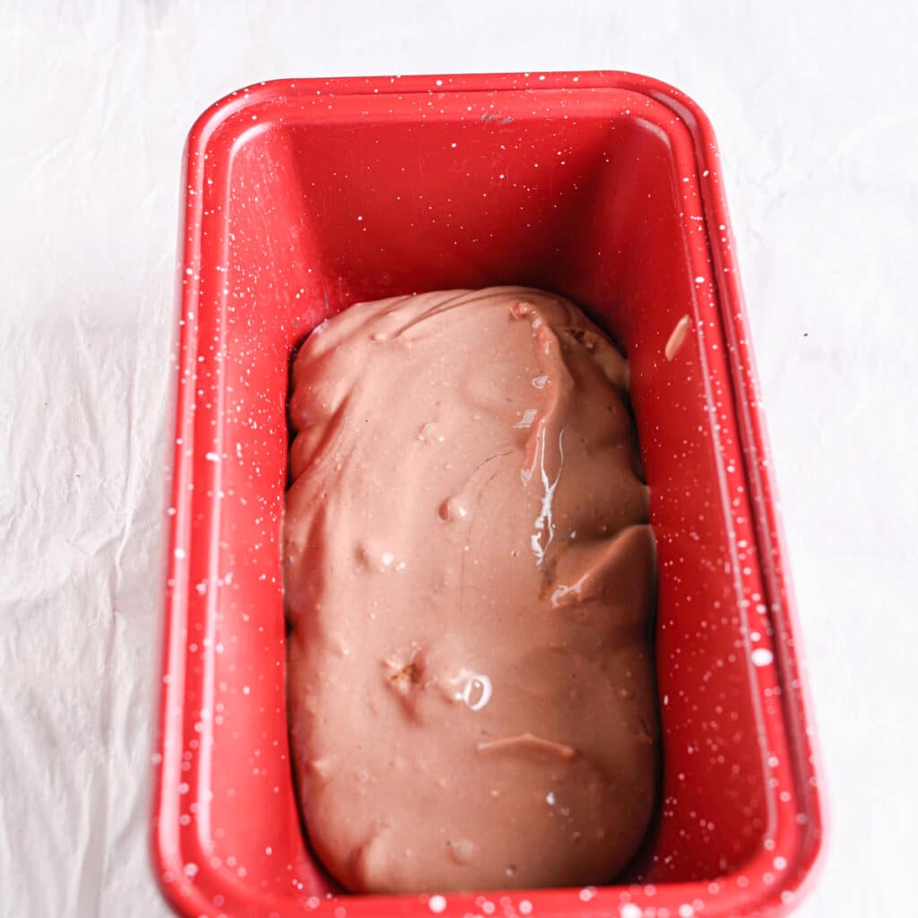Freshly blended chocolate cottage cheese ice cream evenly spread in a red loaf pan before freezing.