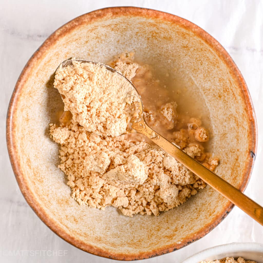 Powdered peanut butter and water in a ceramic bowl ready to be mixed with water.