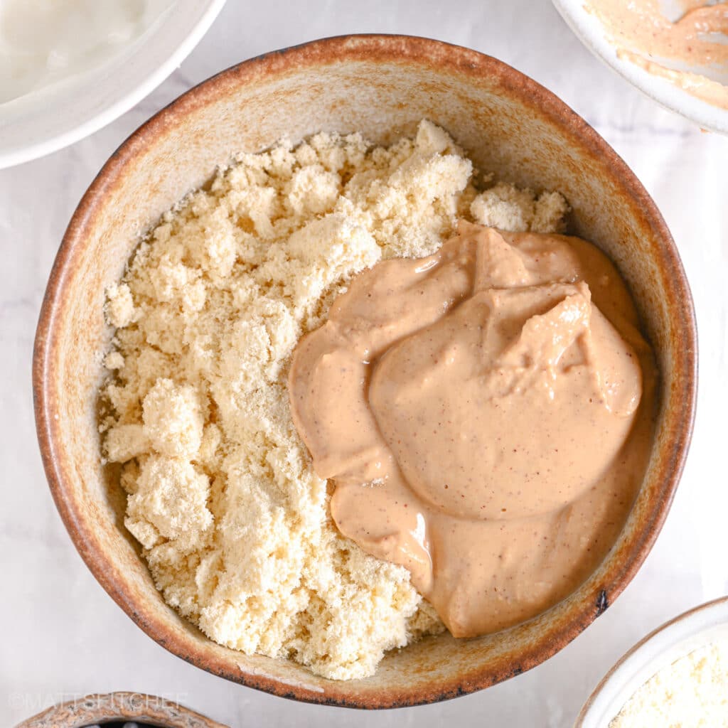 A scoop of creamy peanut butter added to the protein powder in the mixing bowl.