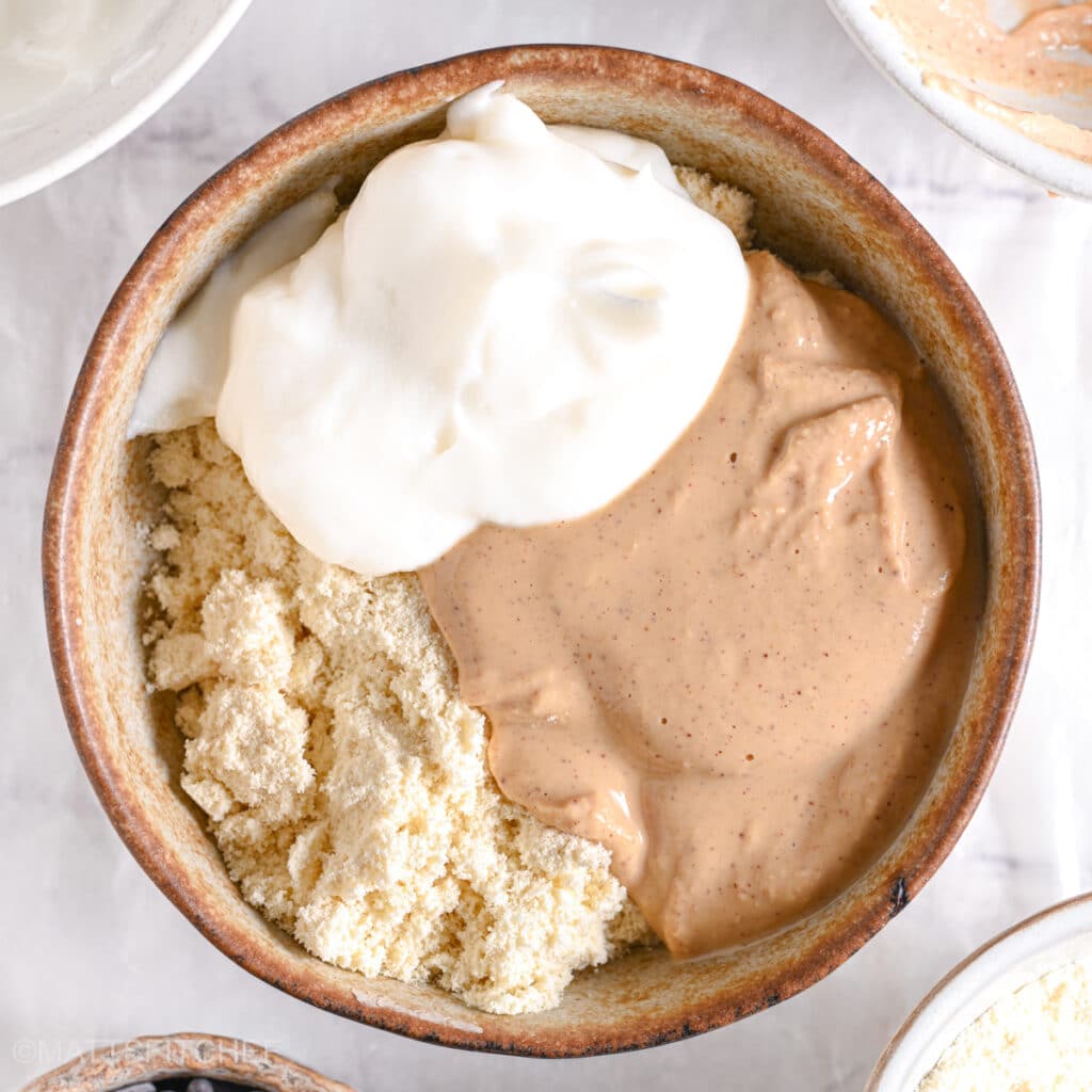 A dollop of thick Greek yogurt sitting on top of protein powder and peanut butter in a bowl.