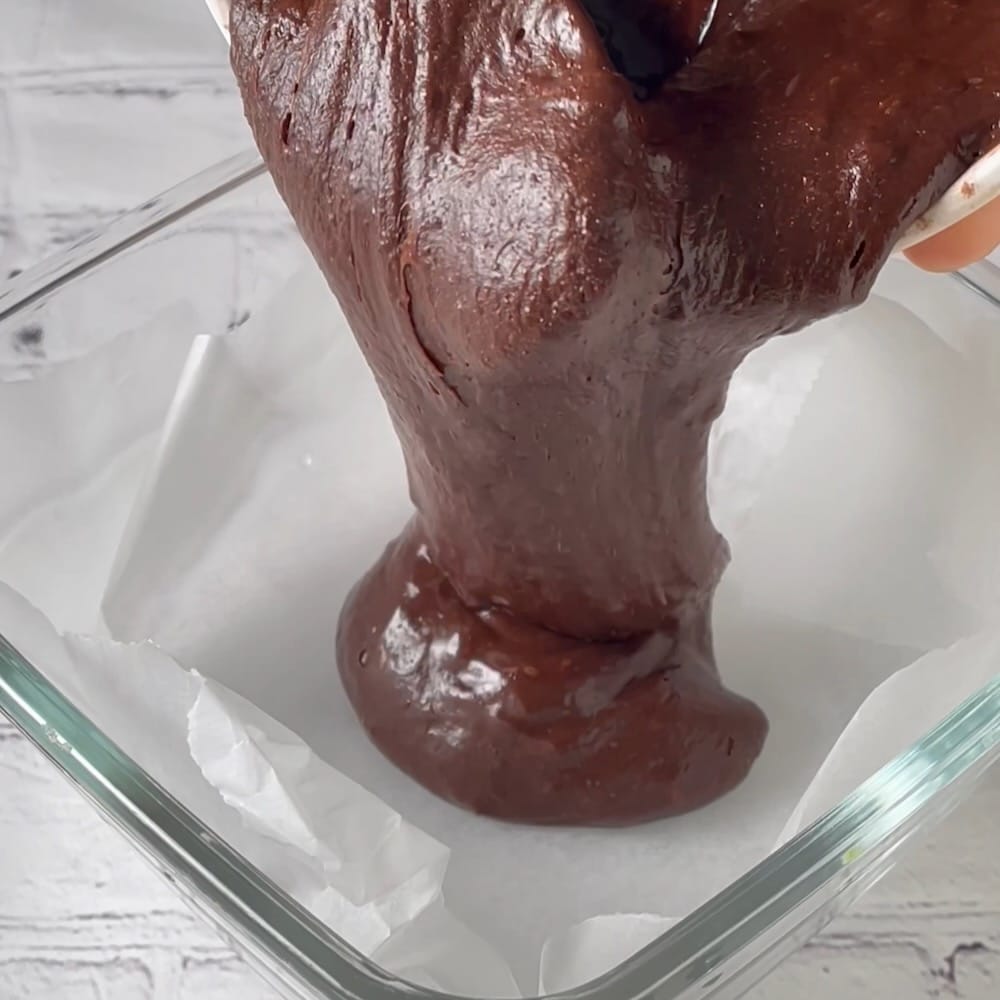 Transferring brownie batter to brownie pan for baking.