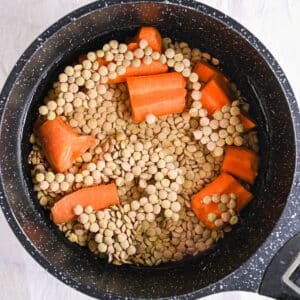 Uncooked French lentils and chopped carrots simmering in a black pot for lentil salad