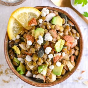 Overhead view of a high protein lentil salad bowl with avocado, cottage cheese, and lemon slices in a ceramic bowl