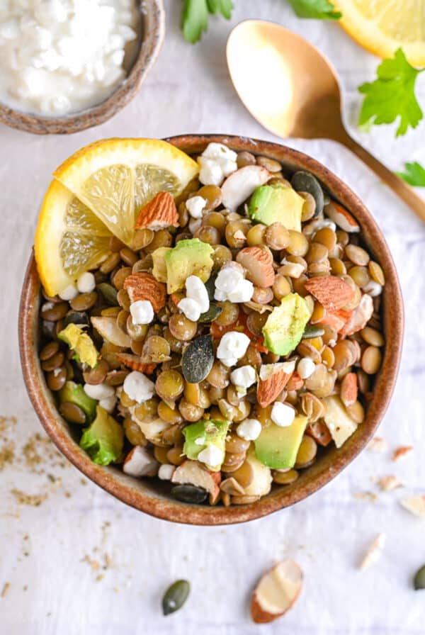 Overhead view of a high protein lentil salad bowl with avocado, cottage cheese, and lemon slices in a ceramic bowl