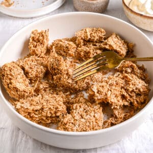 Crushed Weetabix in a bowl with a fork – A white bowl filled with crushed Weetabix, ready to be mixed for an easy overnight Weetabix recipe.