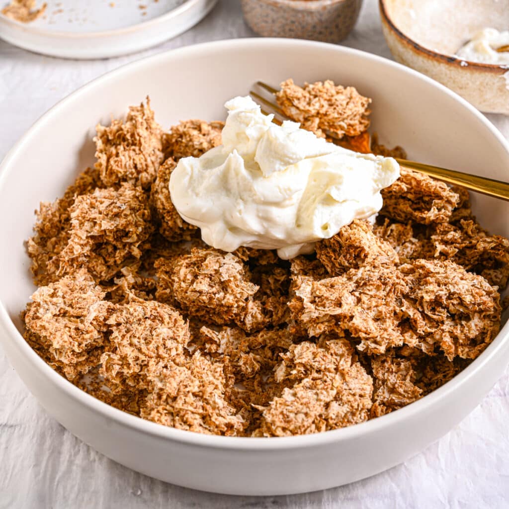 Greek yogurt added to crushed Weetabix – A dollop of thick Greek yogurt on top of crumbled Weetabix, highlighting the creamy texture.