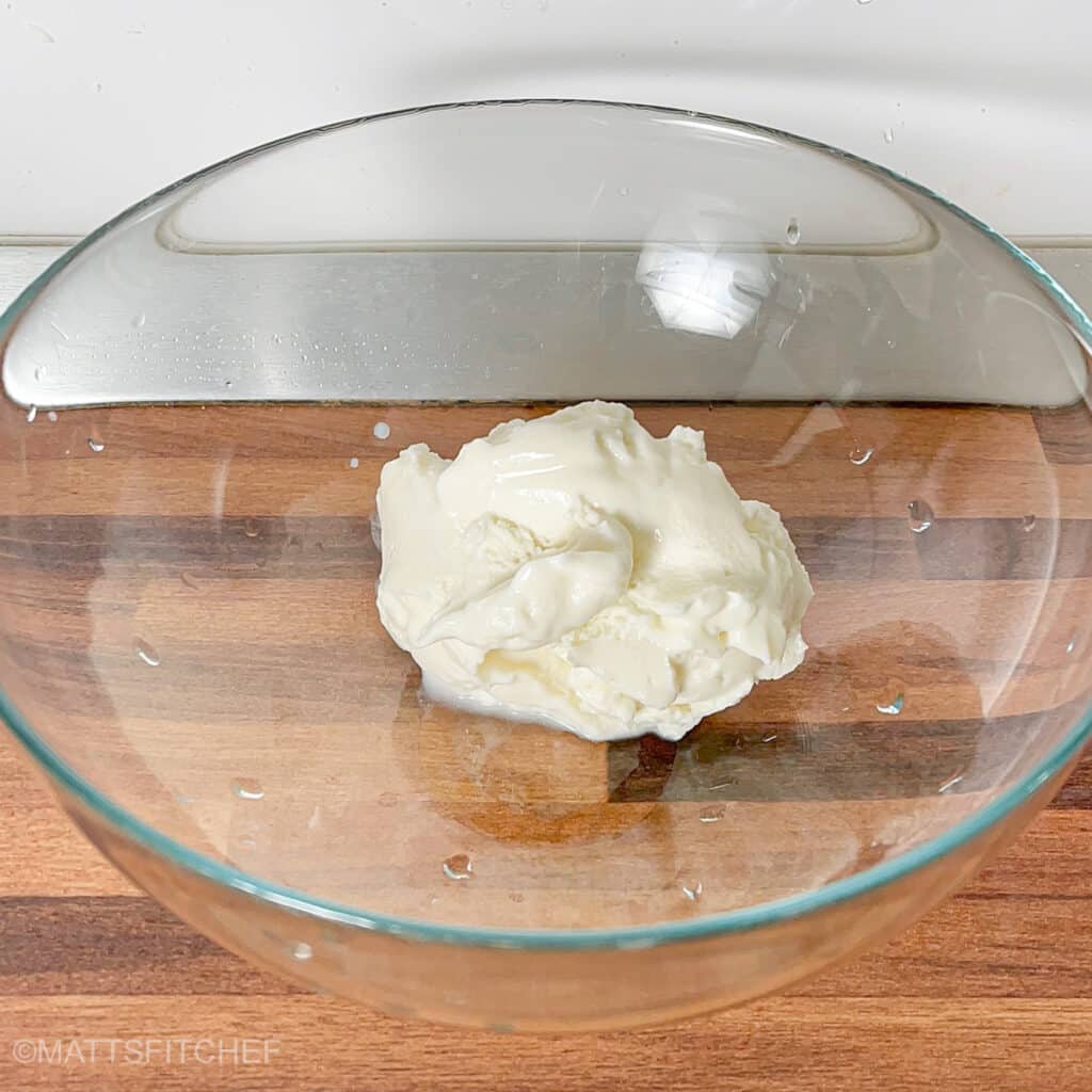 Greek yogurt in a glass mixing bowl on a wooden surface, ready as the base for chocolate protein mousse.