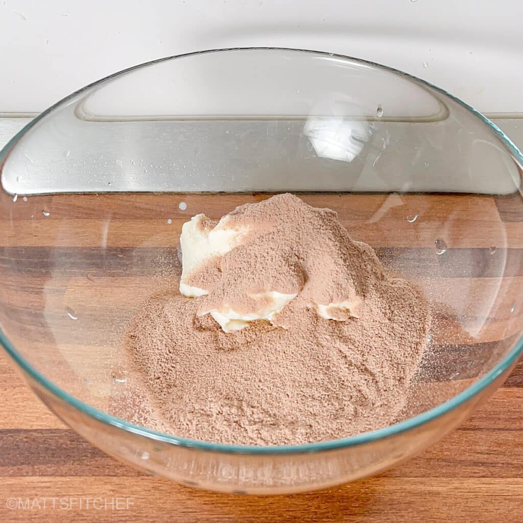 Greek yogurt topped with chocolate protein powder in a bowl, showing the simple two-ingredient mousse preparation.