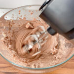 Mixing process of chocolate protein mousse with an electric mixer, blending protein powder and yogurt.