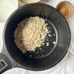 Cooking Rolled Oats in a Black Pot – Dry rolled oats in a speckled black pot, ready to be cooked into a creamy protein oatmeal.