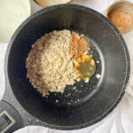 Adding Cinnamon and Maple Syrup to Oats in a Pot – Rolled oats mixed with cinnamon and maple syrup in a black pot for a naturally sweetened oatmeal recipe.