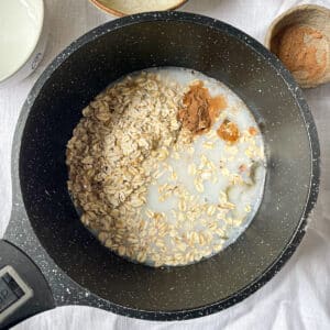 Pouring Milk into a Pot of Oats and Spices – A step-by-step process of making protein oatmeal, with milk added to oats, cinnamon, and maple syrup for extra creaminess.