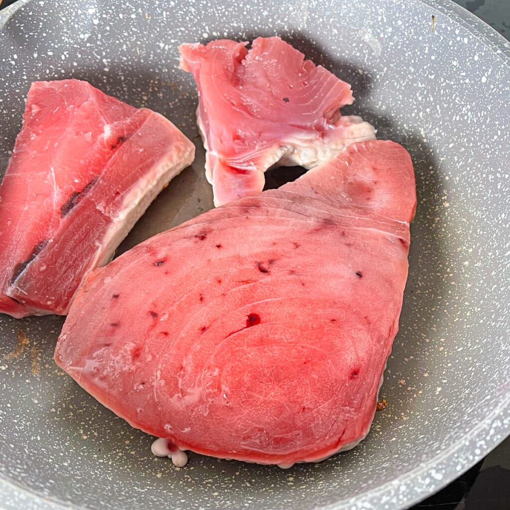 Raw tuna steak in a pan &ndash; Fresh ahi tuna steaks in a non-stick pan, ready to be seared for a quick and healthy meal.