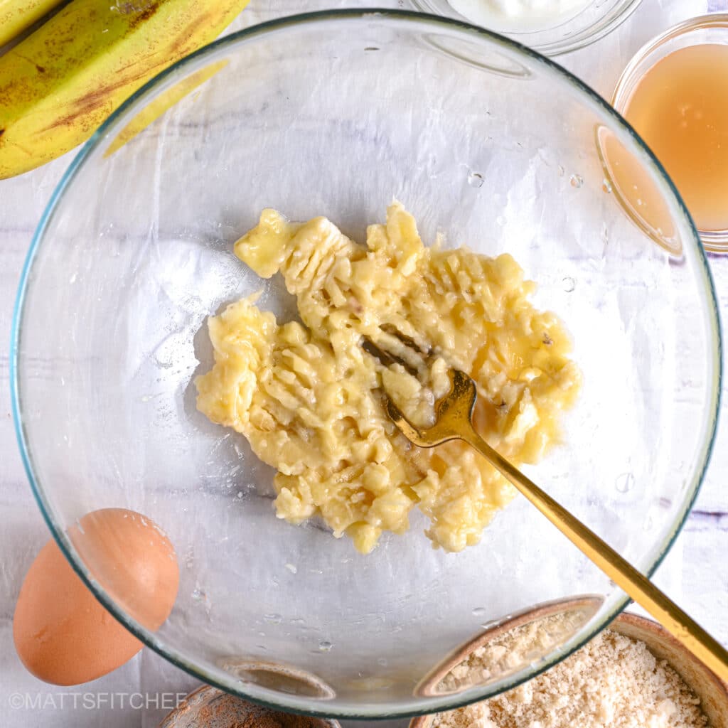 Mashing bananas with a golden fork until smooth to make almond flour banana bread.