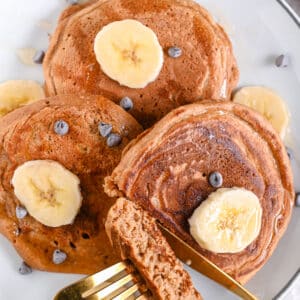 Protein egg white pancakes in a plate, cut and topped with sliced bananas, dark chocolate chips and a drizzle of maple syrup.