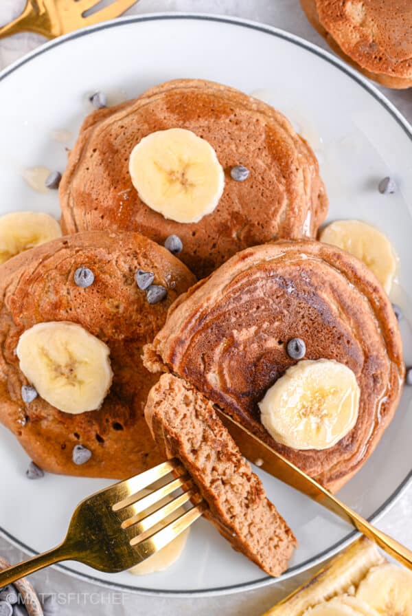 Protein egg white pancakes in a plate, cut and topped with sliced bananas, dark chocolate chips and a drizzle of maple syrup.