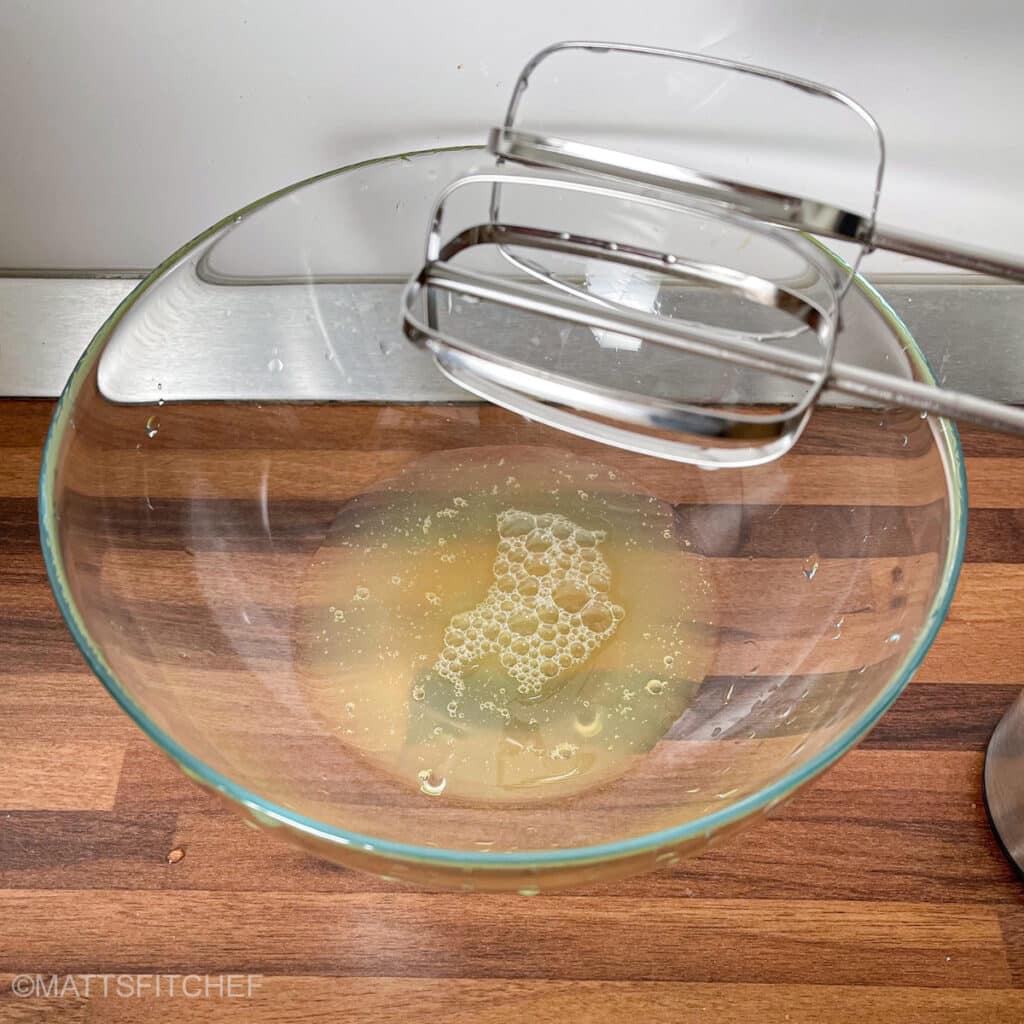 Liquid egg whites in a transparent bowl ready to be beaten with electric mixer.