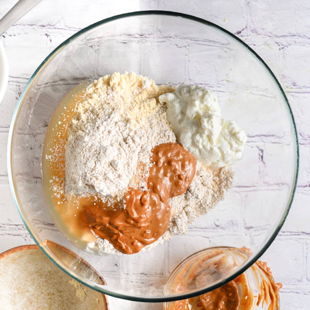 Ingredient for protein balls recipe in a transparent bowl &ndash; protein powder, oat flour, peanut butter, maple syrup and Greek yogurt.