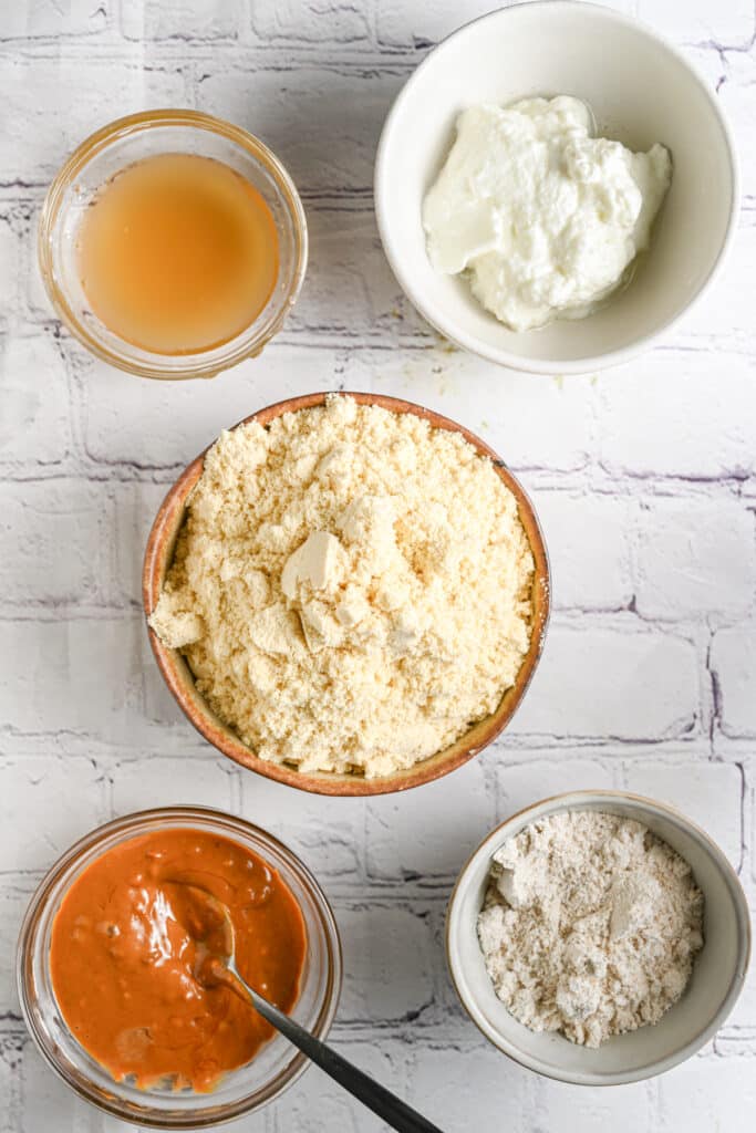 Ingredient for protein balls layered on a flat surface &ndash; protein powder, oat flour, peanut butter, maple syrup and Greek yogurt.