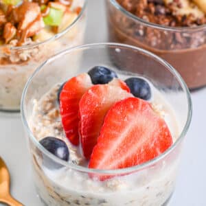 Strawberry overnight oats served in glass and topped with fresh strawberries and juicy blueberries.