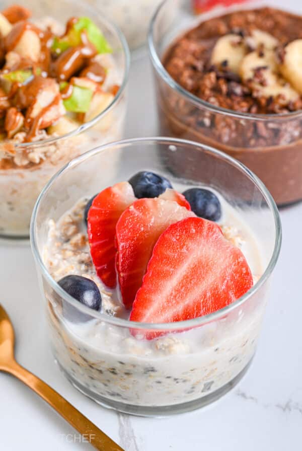 Strawberry overnight oats served in glass and topped with fresh strawberries and juicy blueberries.