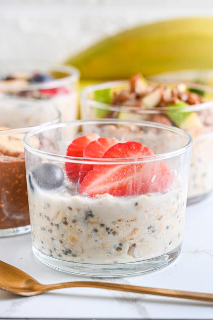 Simple overnight oats served in glass jars, topped with fresh fruit like fresh strawberries, blueberries, apples and bananas