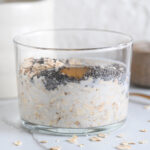 Old fashioned rolled oats, chia seeds, maple syrup and milk in a glass to make porridge