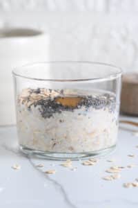 Old fashioned rolled oats, chia seeds, maple syrup and milk in a glass to make porridge