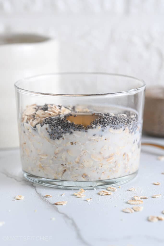 Old fashioned rolled oats, chia seeds, maple syrup and milk in a glass to make porridge