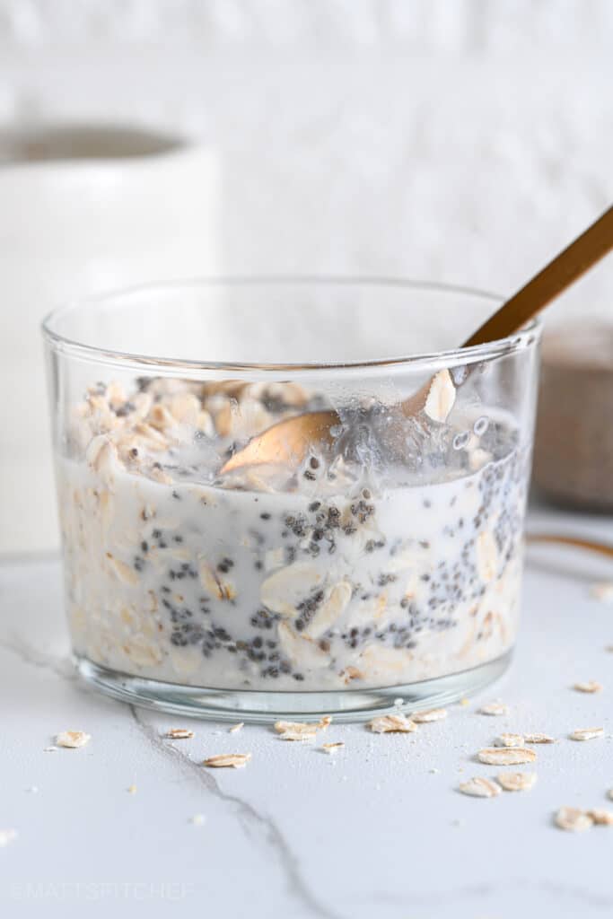 Mixing ingredients in a glass with a golden spoon to before refrigerating oatmeal