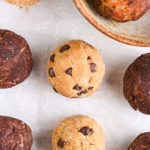 Chocolate chip protein balls, both cocoa-coated and uncoated, scattered on a neutral background, with a ceramic bowl partially visible.