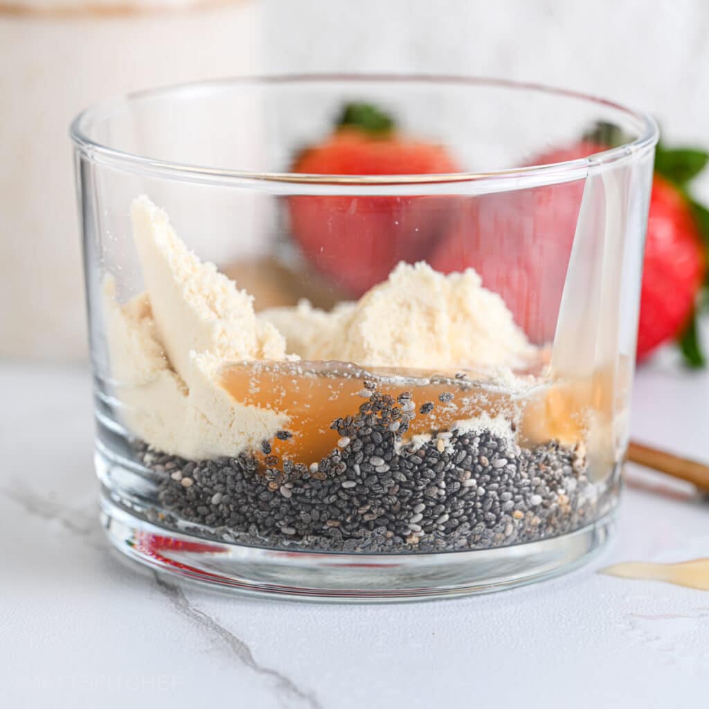 Chia seeds, protein powder and maple syrup in a transparent glass, ready to add milk and stir.