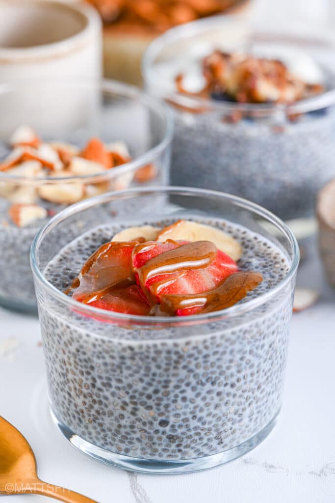 Serving glasses with high protein chia pudding, prepared with brown chia seeds, protein powder and almond milk. Each pudding has a different toppings, one mixed berries, the other blueberries with yogurt and the other chopped almonds