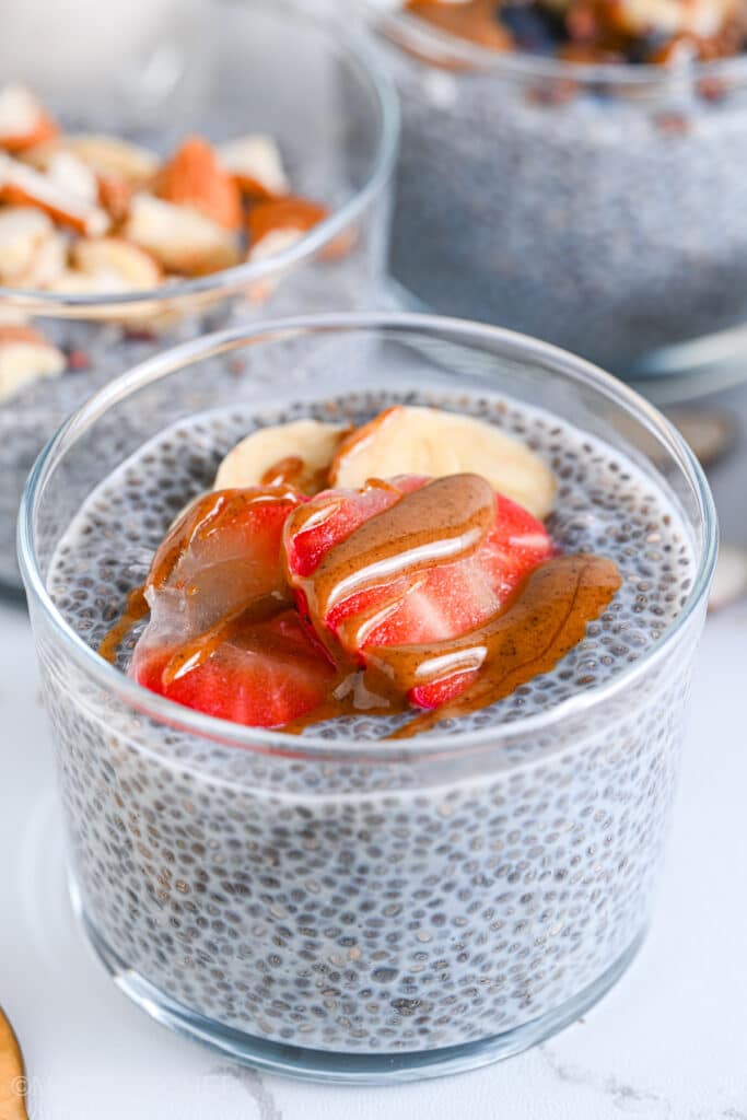 Close-up of high protein chia pudding, topped with sliced strawberries, bananas, and almond butter. Perfect as a low carb and dairy-free snack or dessert.