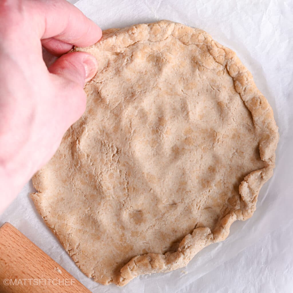 Rolling dough with rolling pin and hands, crafting the borders with fingers.
