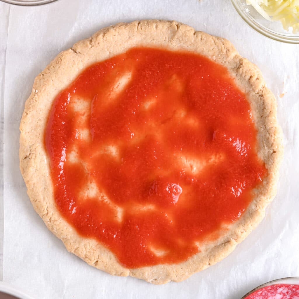 Greek yogurt pizza base topped with homemade pizza sauce before adding cheese and toppings.