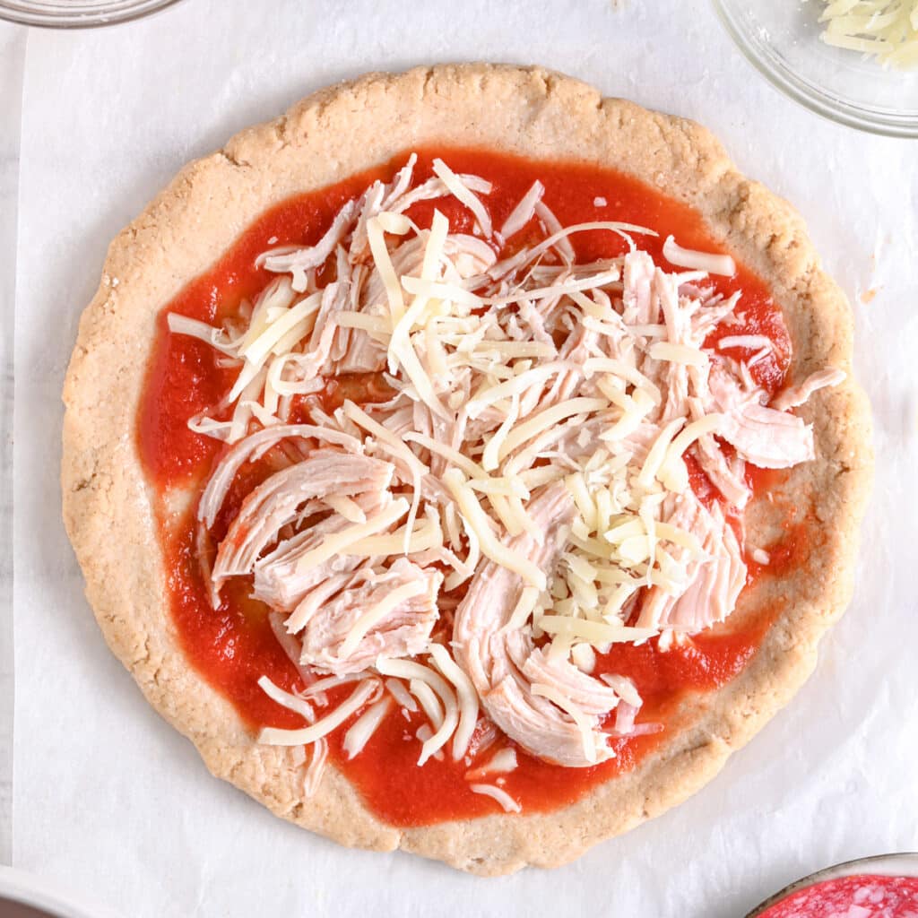 Protein pizza crust topped with pizza sauce, shredded cheese and shredded chicken ready baking