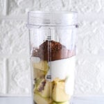 Bullet blender containing chunks of apple, plain Greek yogurt and unsweetened cocoa powder, ready to blend into a chocolate pudding.