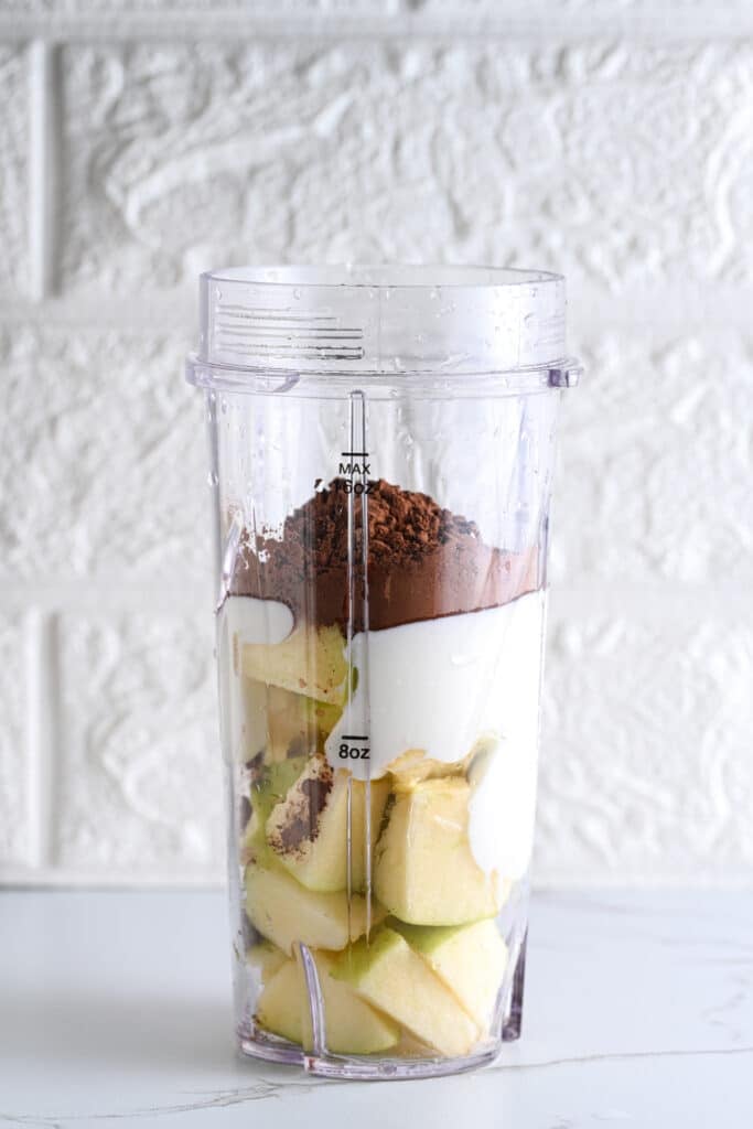 Bullet blender containing chunks of apple, plain Greek yogurt and unsweetened cocoa powder, ready to blend into a chocolate pudding.