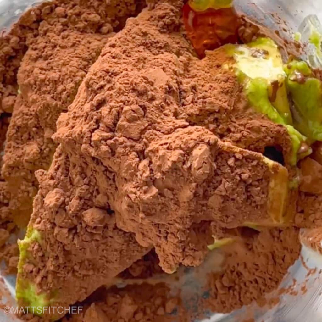 Diced avocados, unsweetened cocoa powder and maple syrup in a blender, ready to pulse until smooth