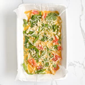 Top view of unbaked cottage cheese egg casserole with spinach, sprinkled with shredded cheese on top.