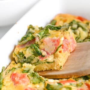 Slice of baked cottage cheese eggs from front, with spinach and diced tomatoes