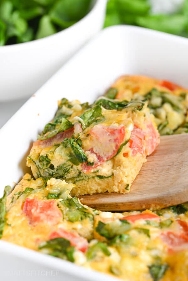 Slice of baked cottage cheese eggs from front, with spinach and diced tomatoes
