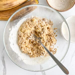 Mixing mashed banana and peanut butter with rolled oats, using a fork