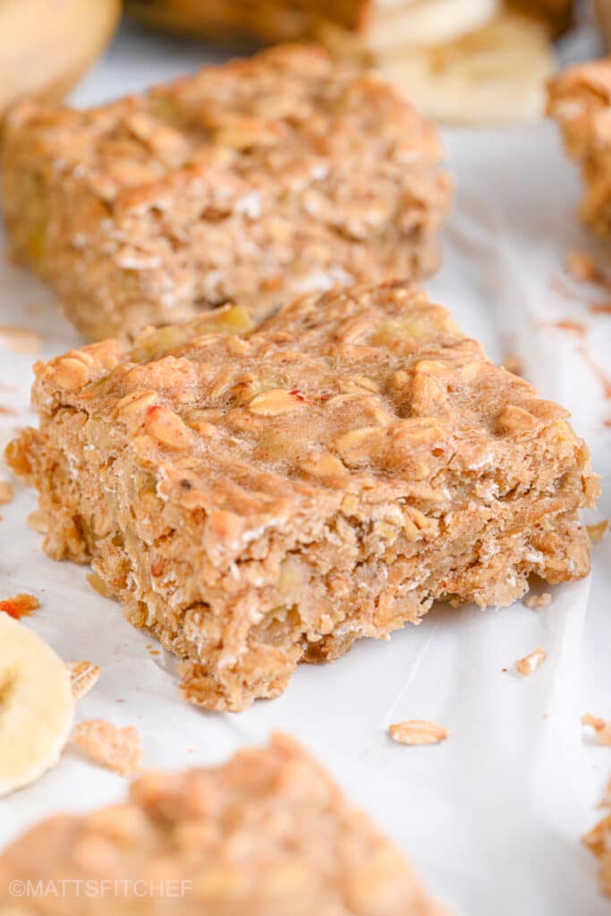 Close-up of a banana oat square, highlighting the chewy texture and with ripe bananas shown in the background.