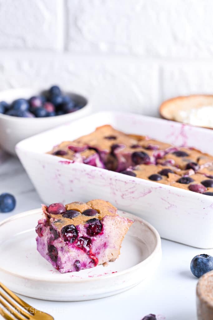 Side view of blueberry cottage cheese breakfast bake, with fresh blueberries and creamy cottage cheese in background