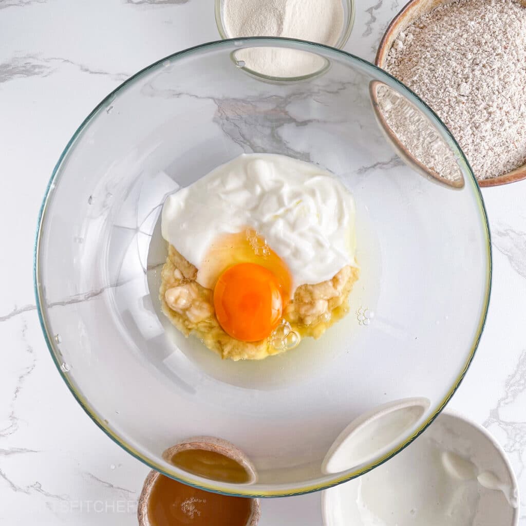 Mashed banana, egg, blended cottage cheese and vanilla extract in a bowl, ready to mix.