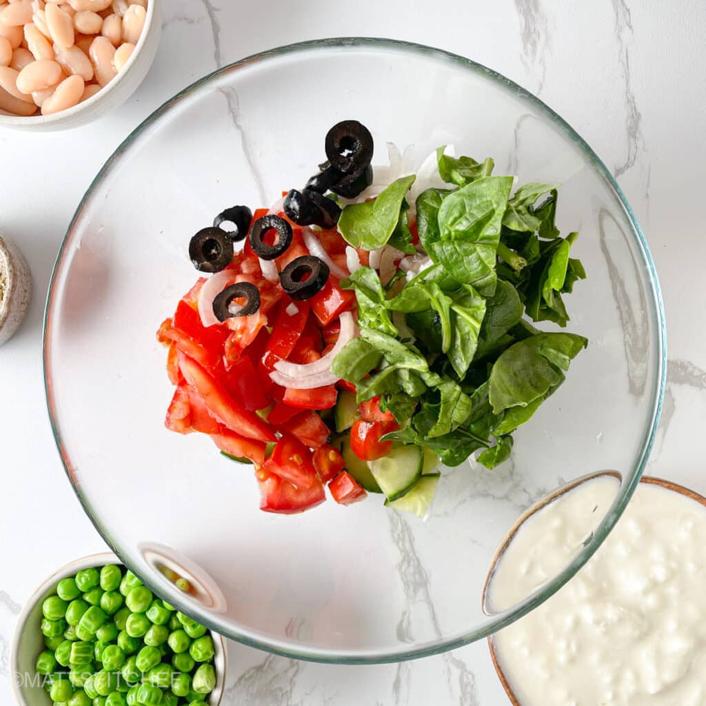 Vegetables added to a glass bowl, ready to combine with protein-packed white beans and peas