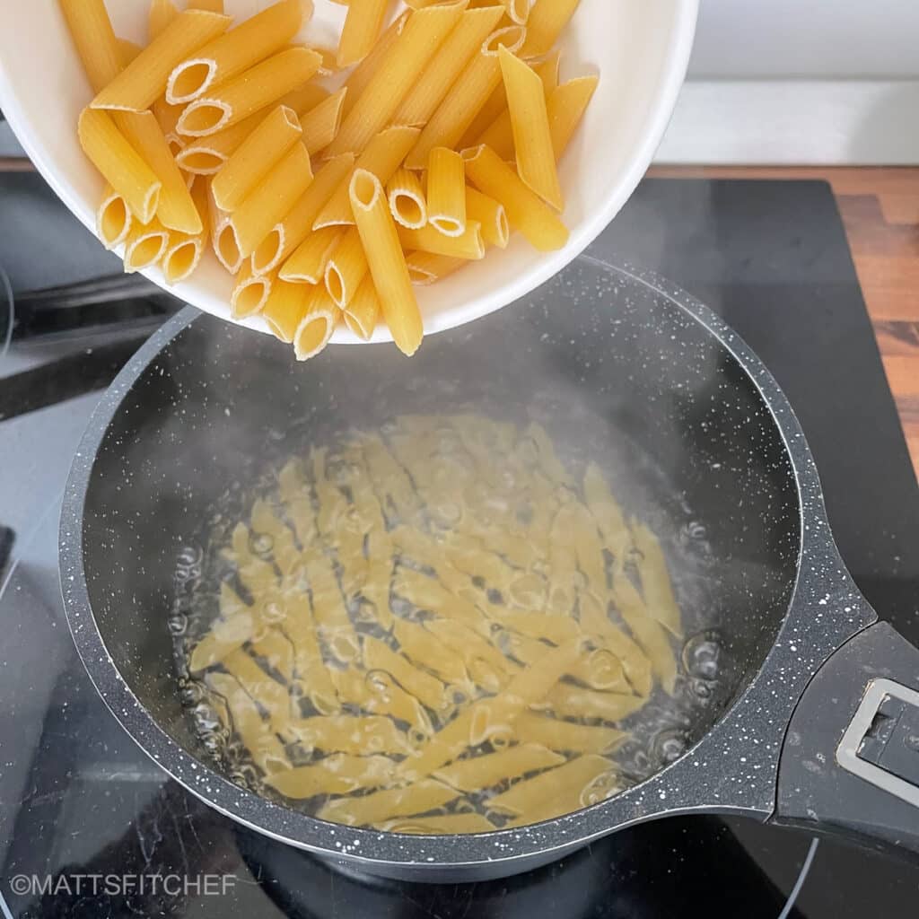 Adding penne to boiling water in a pot, first step of this low calorie pasta salad recipe