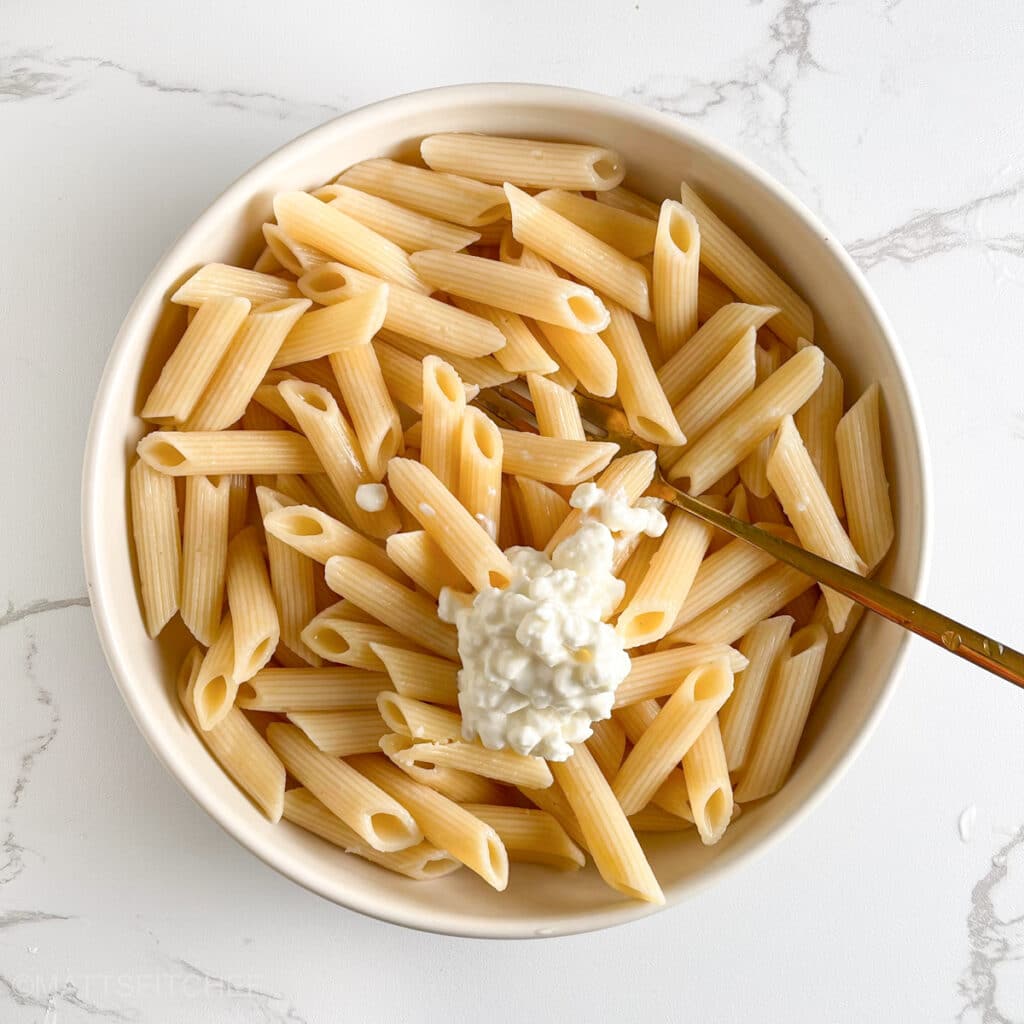 Creamy nonfat cottage cheese being added to the cooked pasta in a bowl, used for creaminess, flavor and protein.